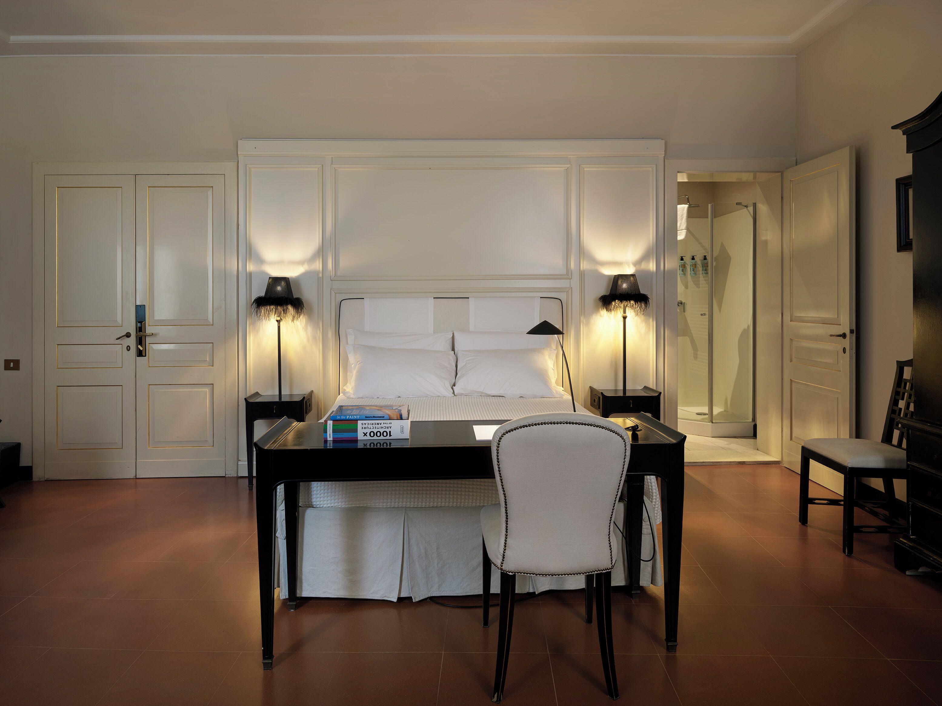 A hotel room with a bed, bedside lamps, a desk with a chair, and a TV.