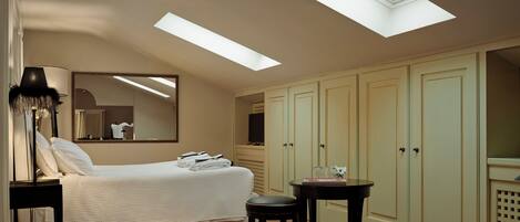 A bedroom with a skylight, a bed, a nightstand, a chair, a table, and a wardrobe.