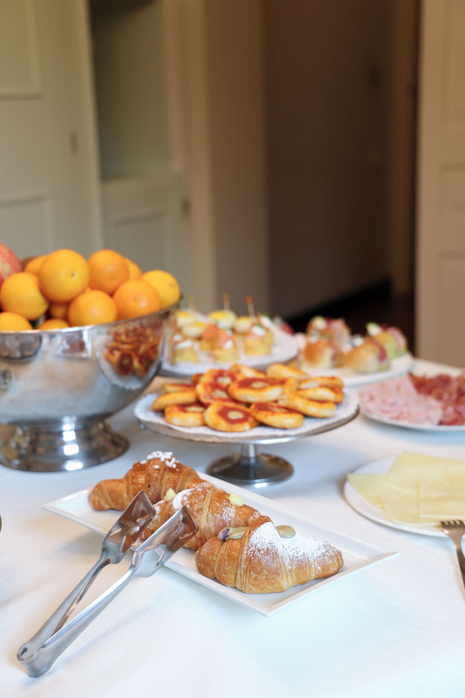 Una mesa de buffet con diversos alimentos, como frutas, pasteles y una fuente de cruasanes.