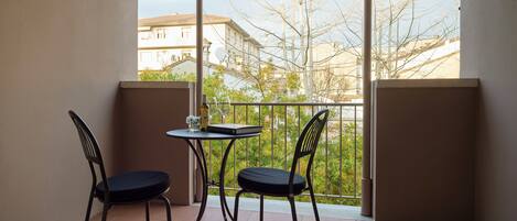 A balcony with two chairs and a small table, overlooking a residential area with trees and buildings.