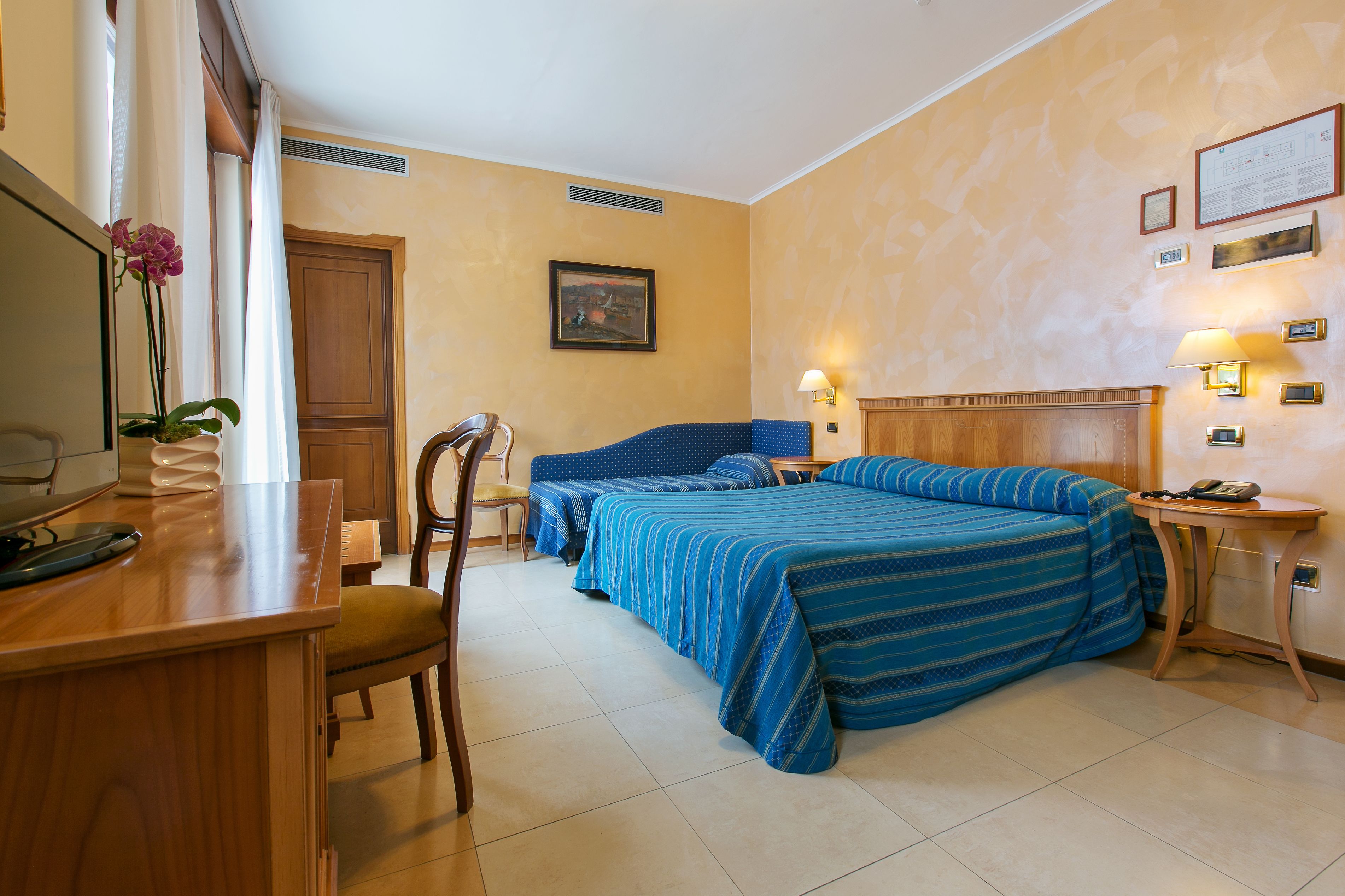 Une chambre d’hôtel avec un lit, un bureau, une chaise, une lampe et un tableau au mur.