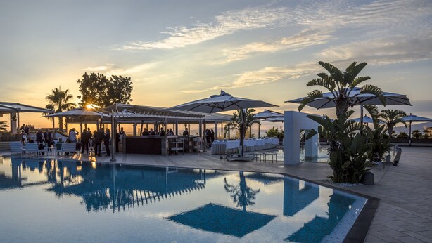 A pool area with lounge chairs and umbrellas, surrounded by palm trees and a sunset view. - Grand Hotel Moon Valley (Vico Equense)