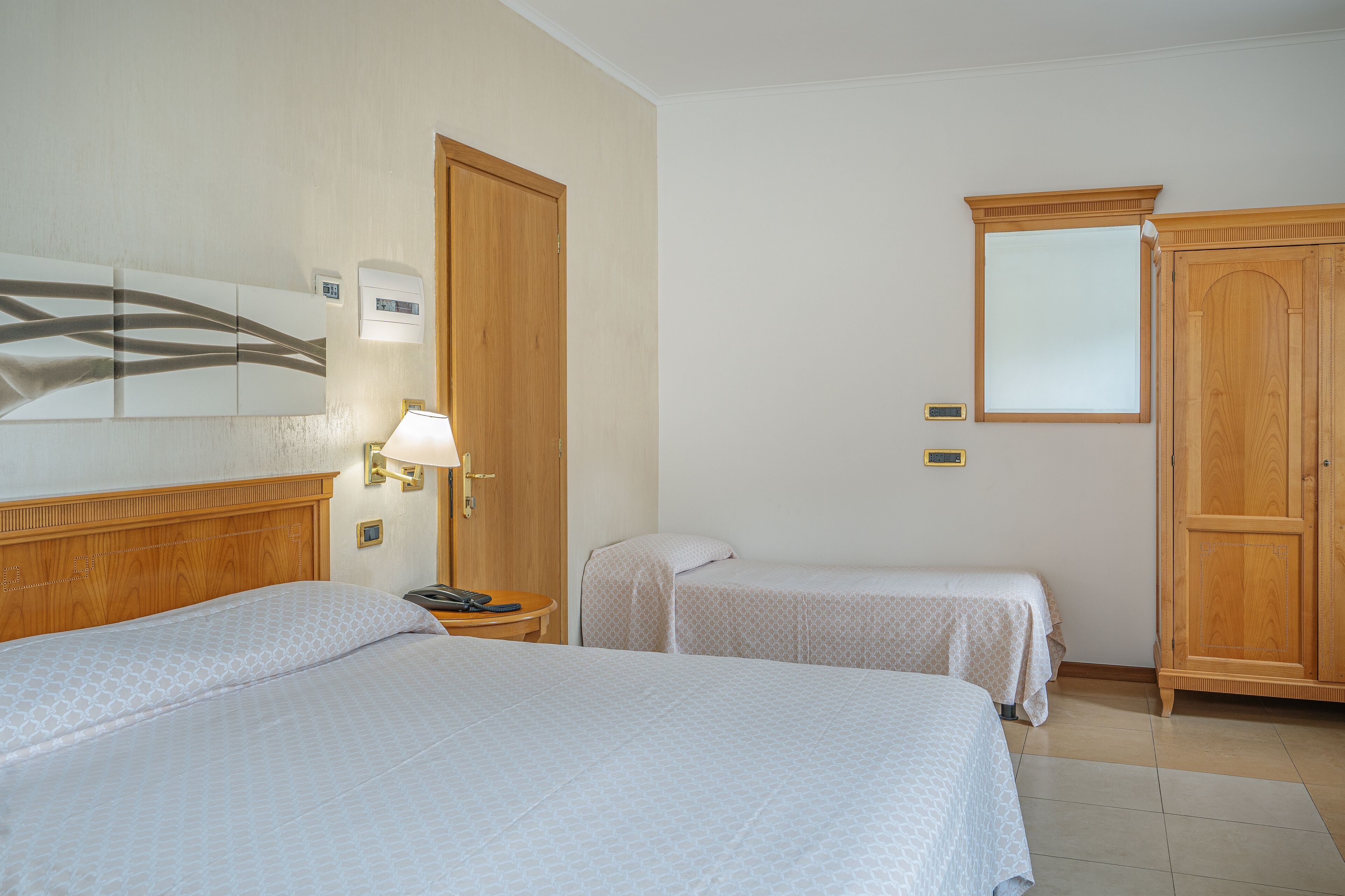 Habitación de hotel con dos camas, un armario de madera, una mesita de noche con lámpara y un equipo de aire acondicionado de pared.