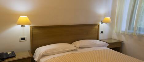 A hotel room with a wooden headboard, two bedside lamps, a telephone on the nightstand, and a patterned bedspread.