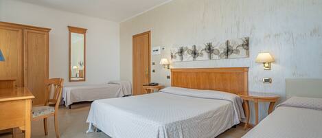 A hotel room with two beds, a wooden desk, a chair, a mirror, and a wall-mounted lamp.