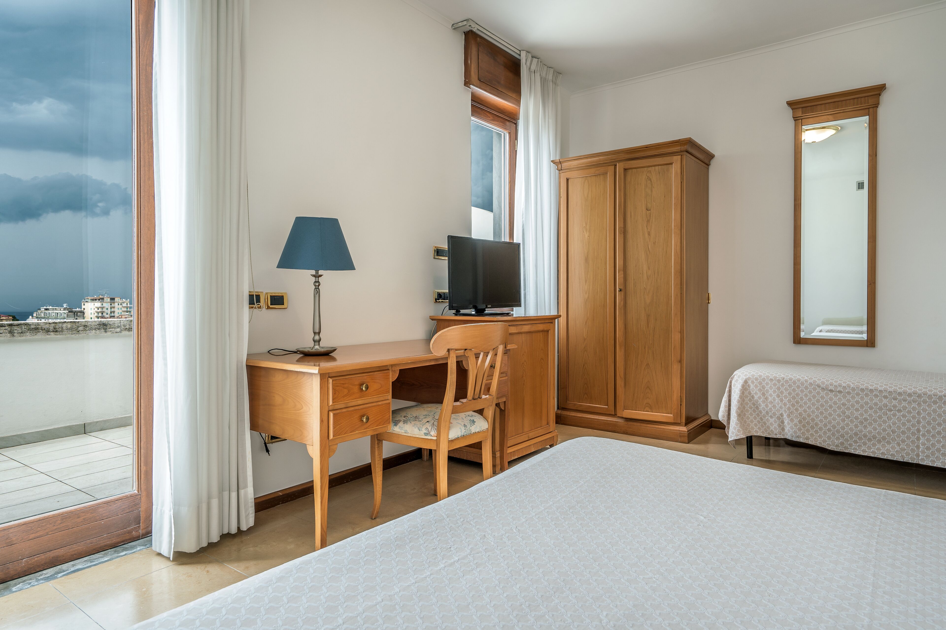 Een hotelkamer met een bed, een bureau met stoel, een televisie, een kledingkast en een raam met gordijnen.
