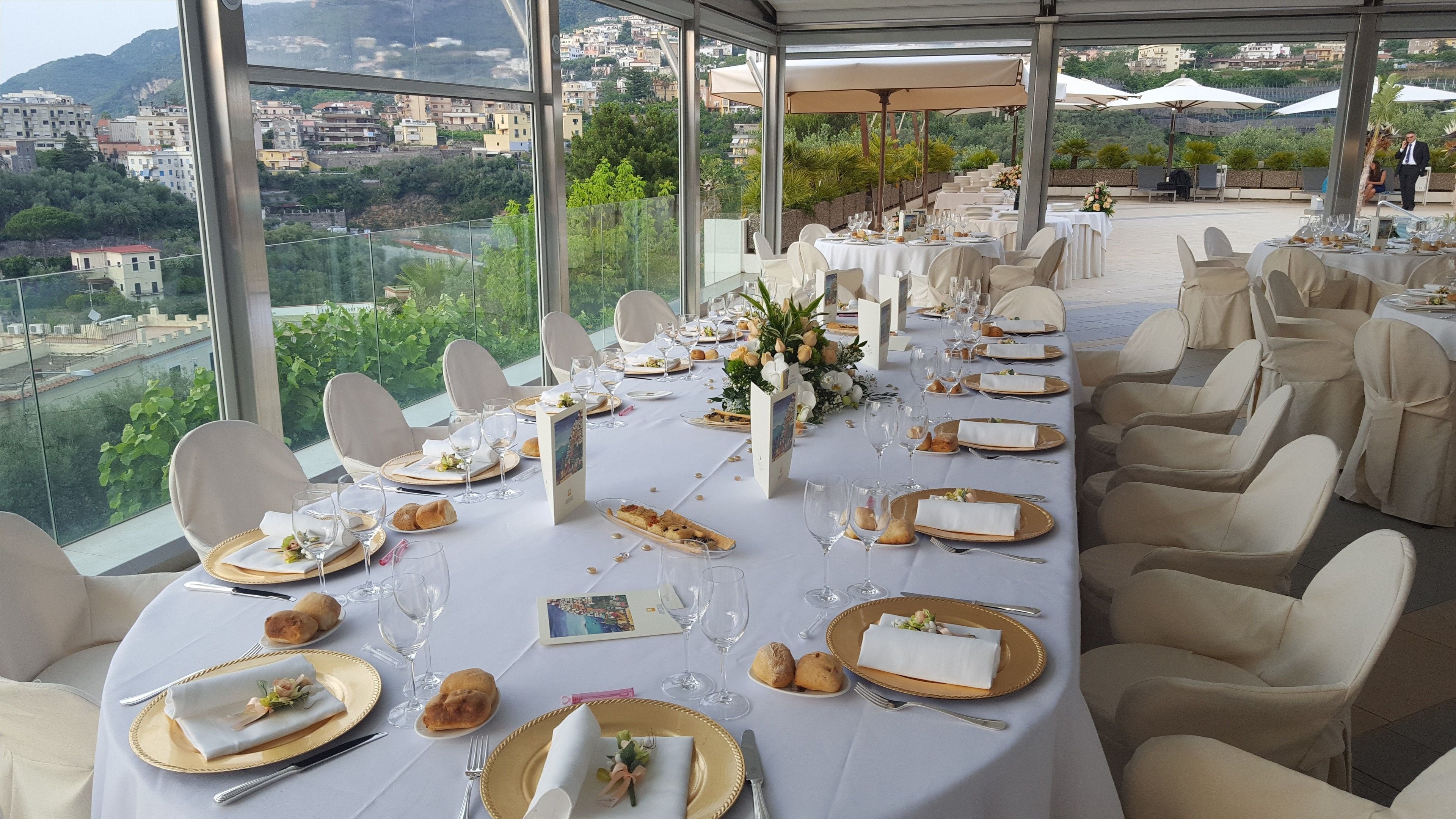 A long table set for a formal event with white tablecloths, gold chargers, and white napkins.