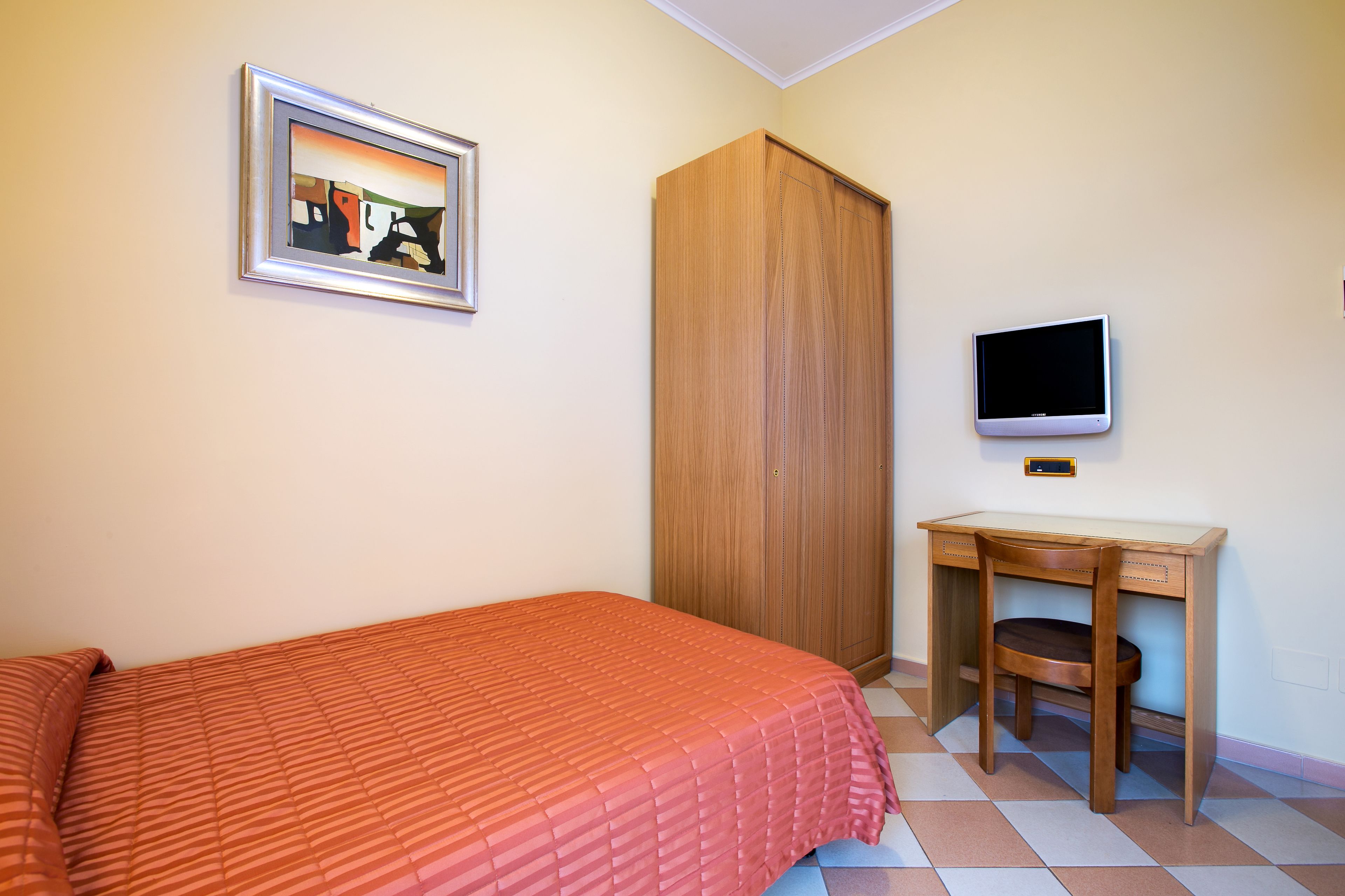 Un dormitorio con una cama, un armario de madera, un escritorio con silla, un televisor y un cuadro en la pared.