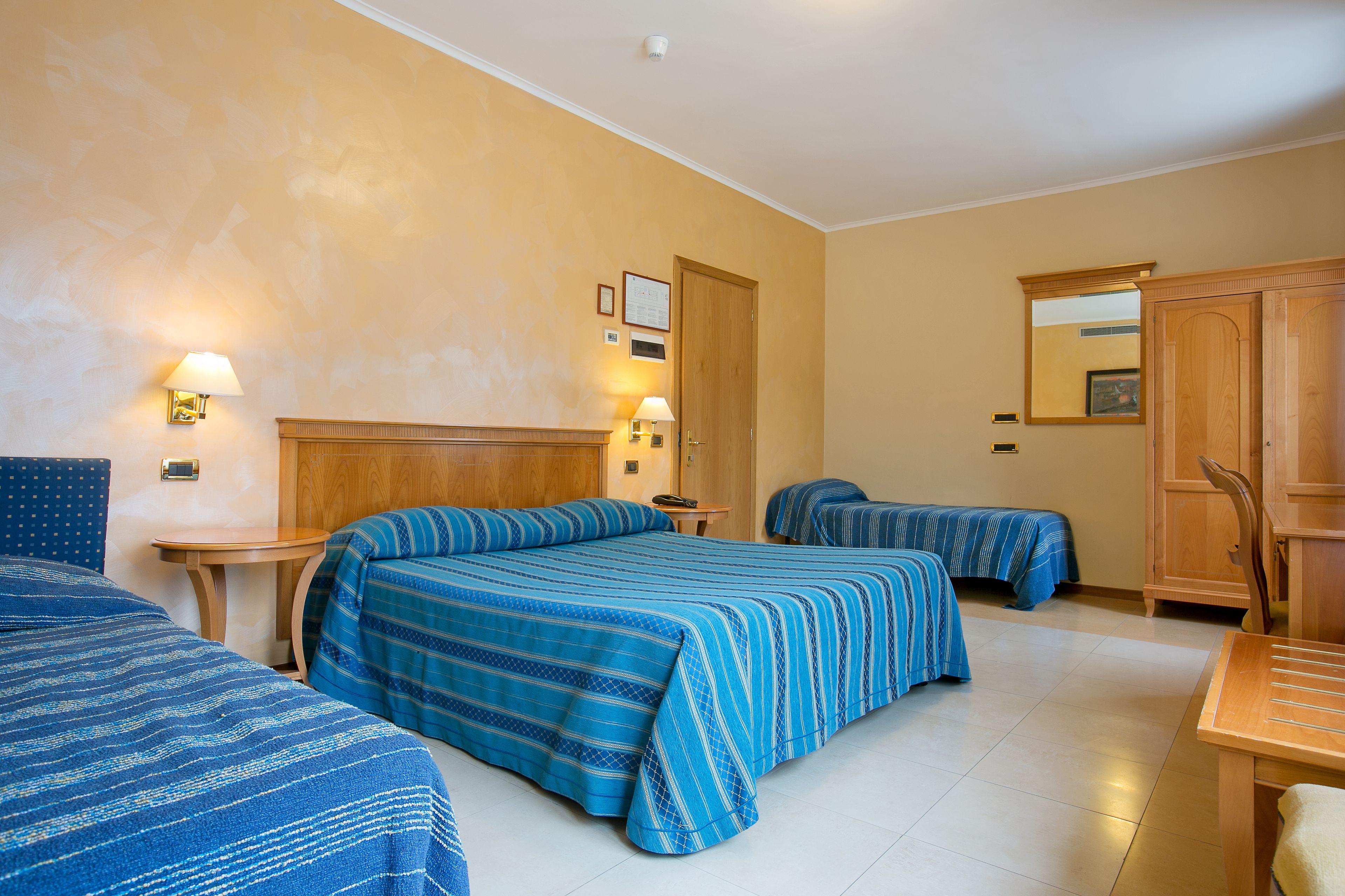 Habitación de hotel con dos camas, cabecera de madera, una mesita, una silla y un armario.