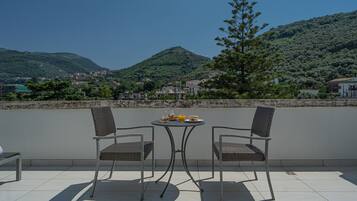 Una terraza con dos sillas de mimbre y una mesita redonda, con vistas a una colina con edificios.