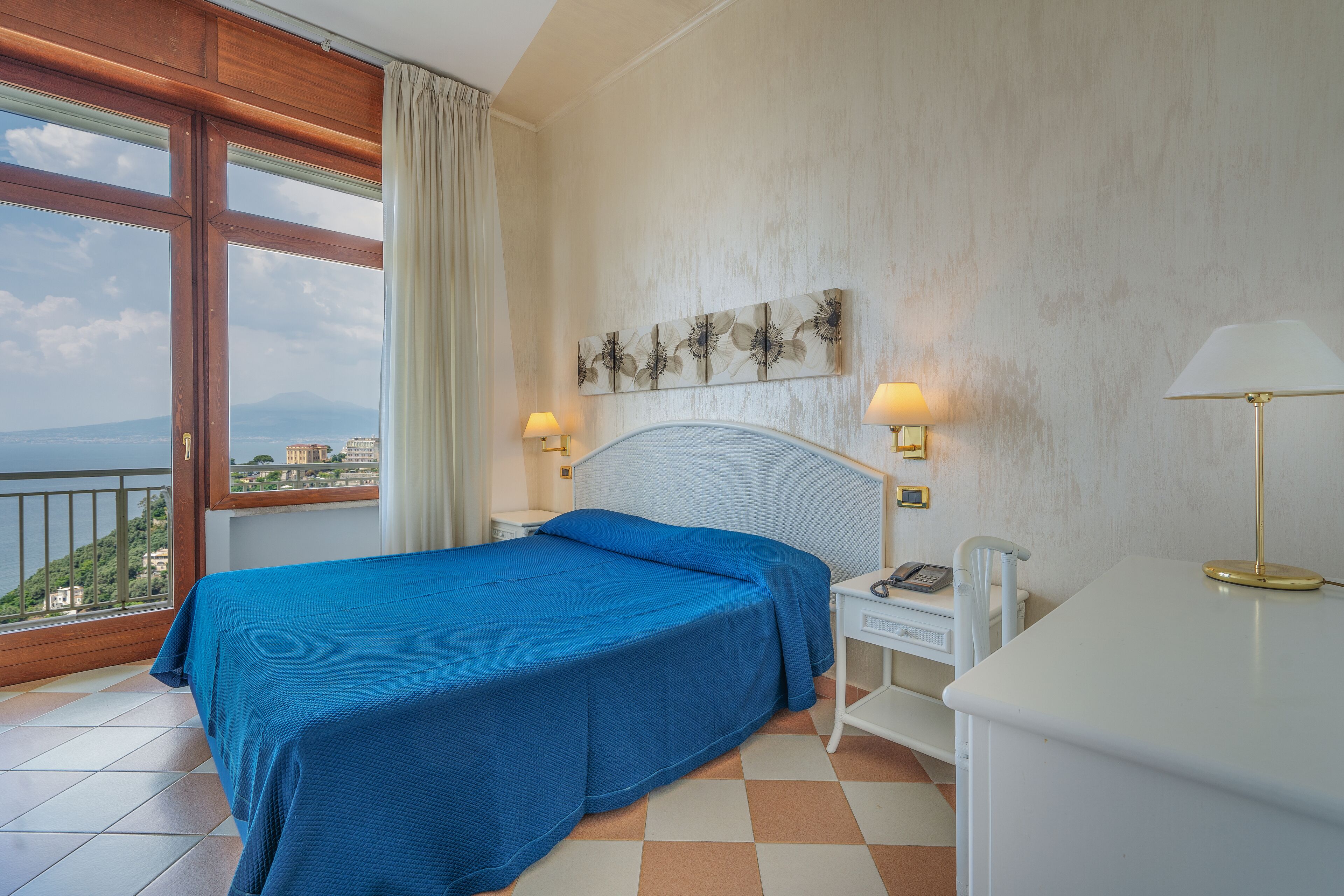 A hotel room with a bed, bedside lamps, a desk, and a view of the city.