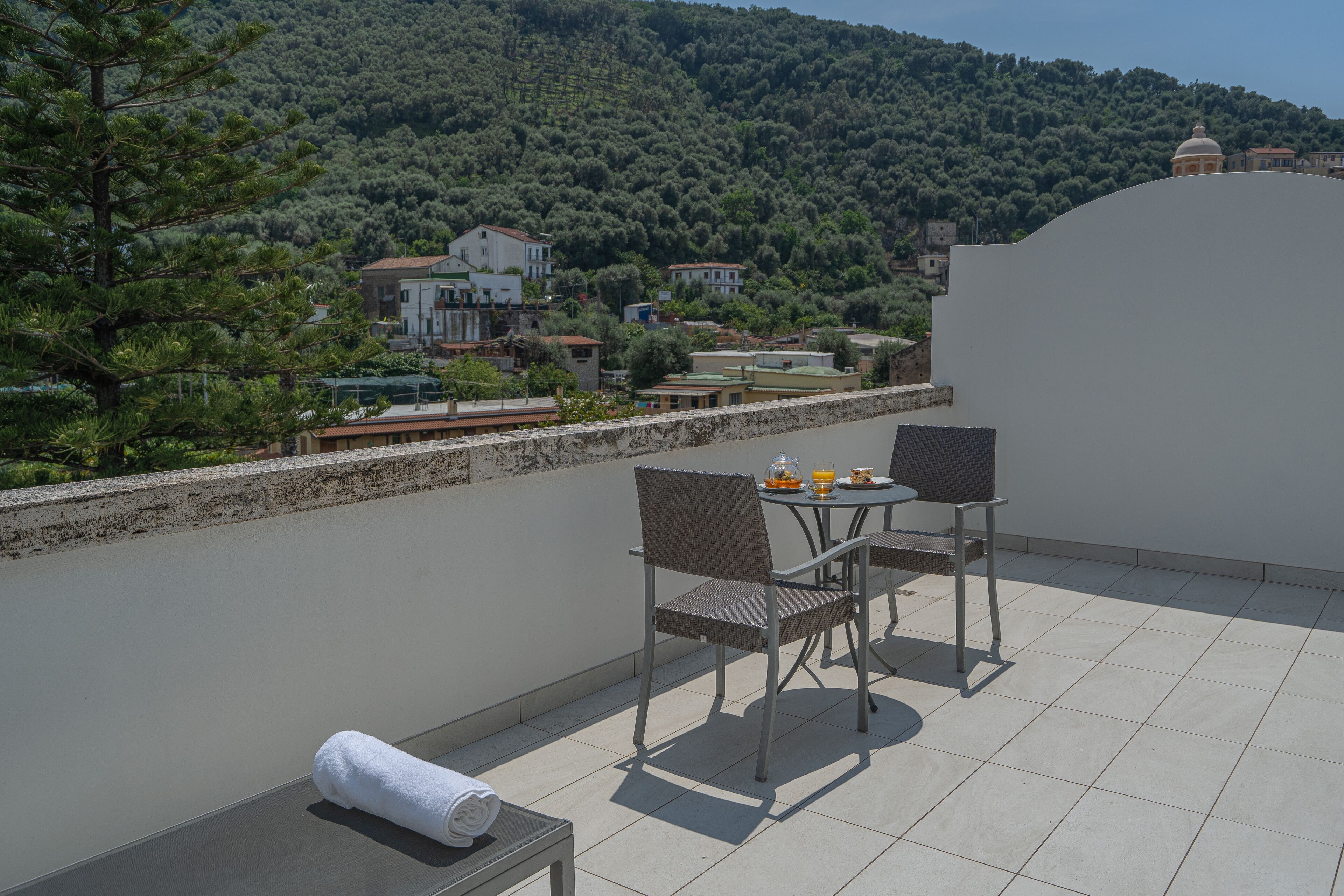 A terrace with a table and chairs, a towel, and a view of a hillside with houses.