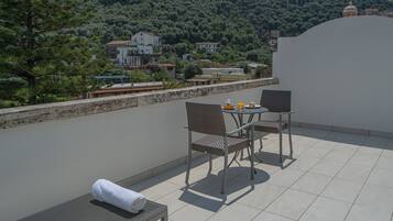 Eine Terrasse mit Tisch und Stühlen, einem Handtuch und Blick auf eine Hügellandschaft mit Häusern.