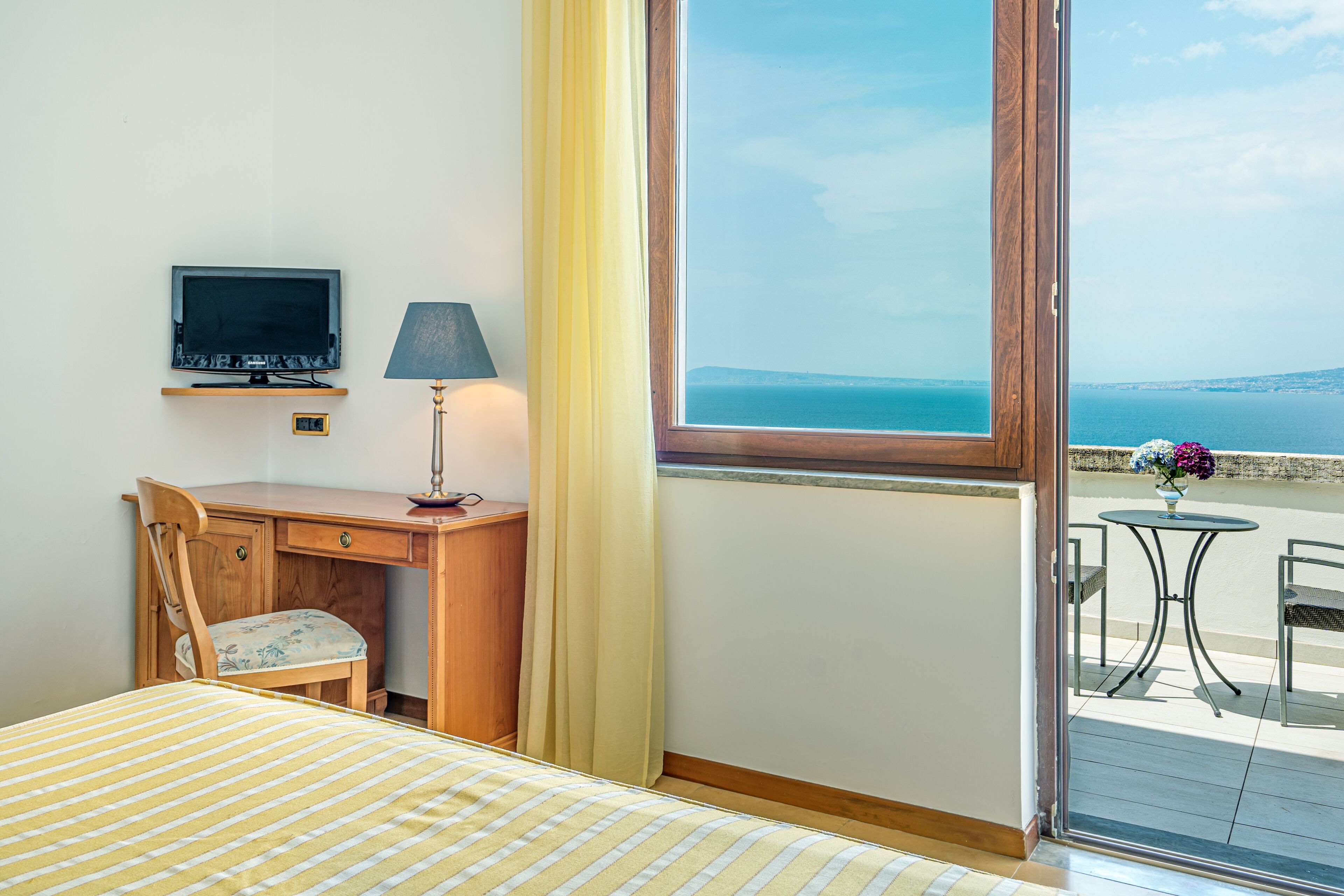 Habitación con cama, escritorio, silla, televisor, lámpara y vista al mar.