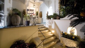 A staircase with ornate railings and a well-lit interior, leading to a room with a large window and a statue. - Gatto Bianco Hotel & SPA (Capri)