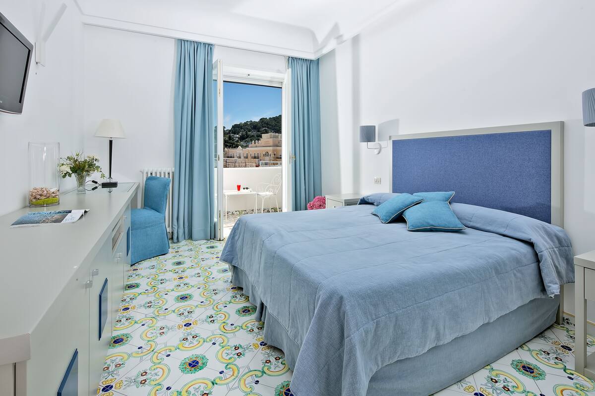A modern hotel room with a bed, a desk, and a view of a coastal landscape.