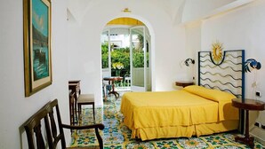 A bedroom with a bed, a chair, a table, and a painting on the wall. - Gatto Bianco Hotel & SPA (Capri)