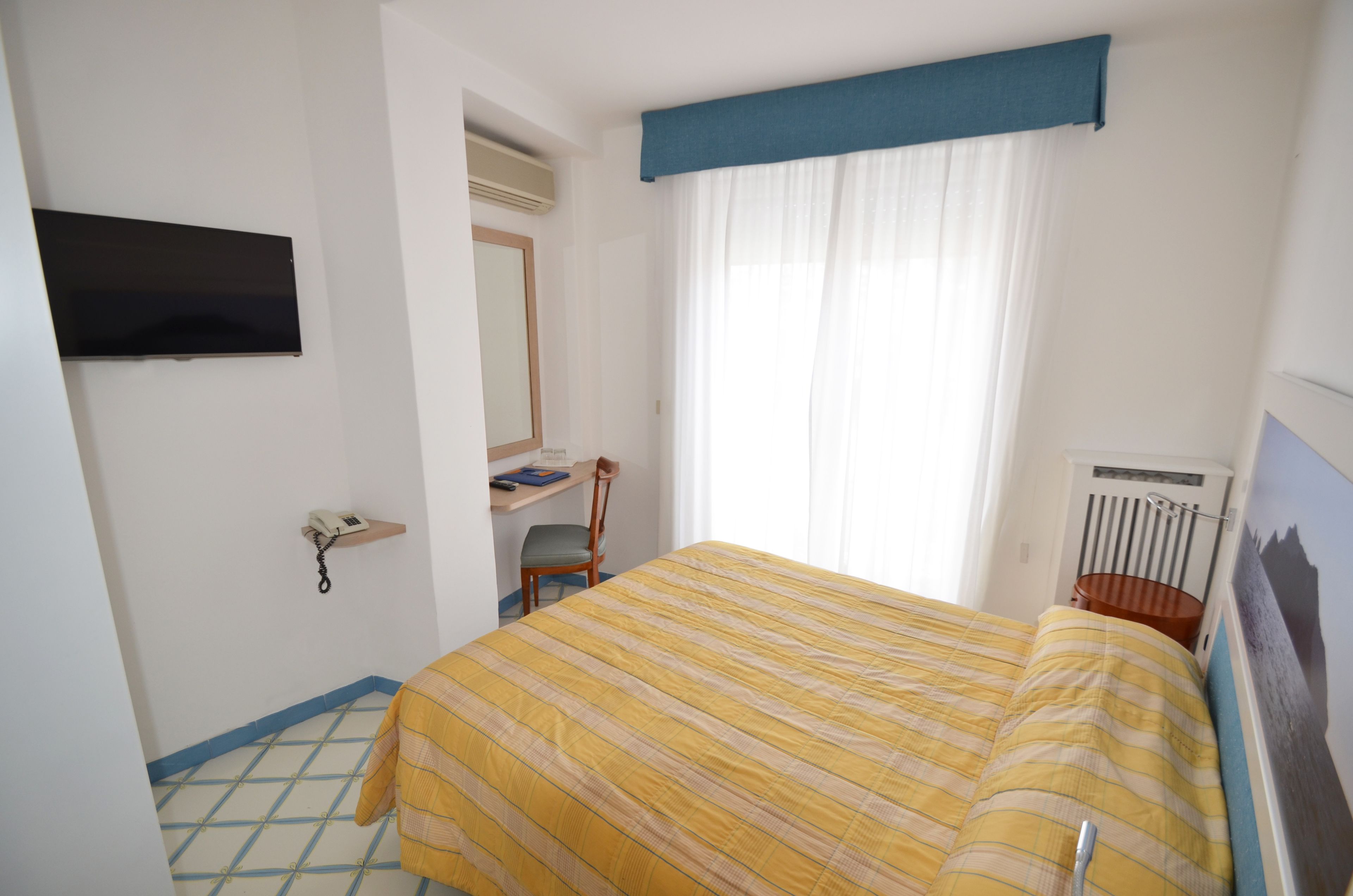 Ein Hotelzimmer mit Bett, Schreibtisch, Stuhl, Fernseher und einem Fenster mit Vorhängen.