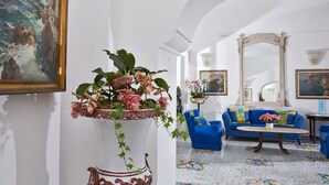 A hallway with a large potted plant, a blue sofa set, and a mirror. - Gatto Bianco Hotel & SPA (Capri)