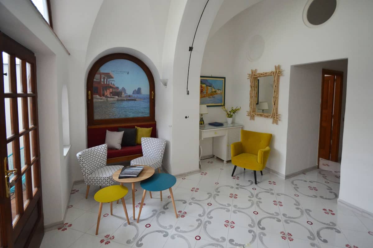 A room with a sofa, patterned chairs, a small table, a desk, and a mirror.