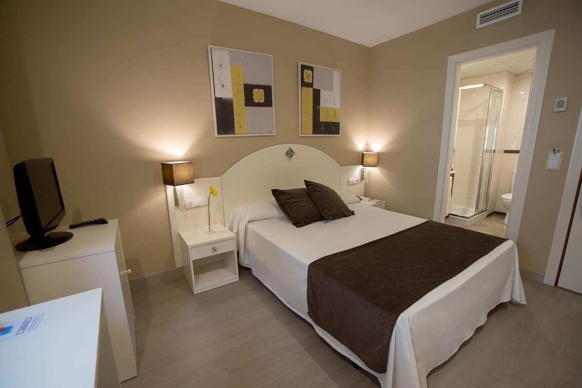 Un dormitorio con cama, mesitas de noche, televisor y una obra de arte en la pared.