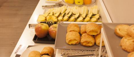A buffet with various food items including fruits, pastries, and bread.