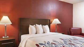 A hotel room with a large bed, two bedside lamps, a red chair, and a nightstand with a lamp.