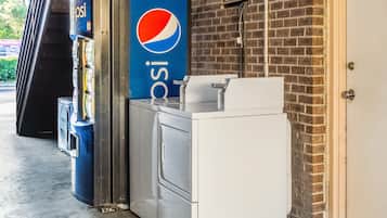 A vending machine and a white appliance, possibly a coffee machine, in a commercial setting with a brick wall and a door.