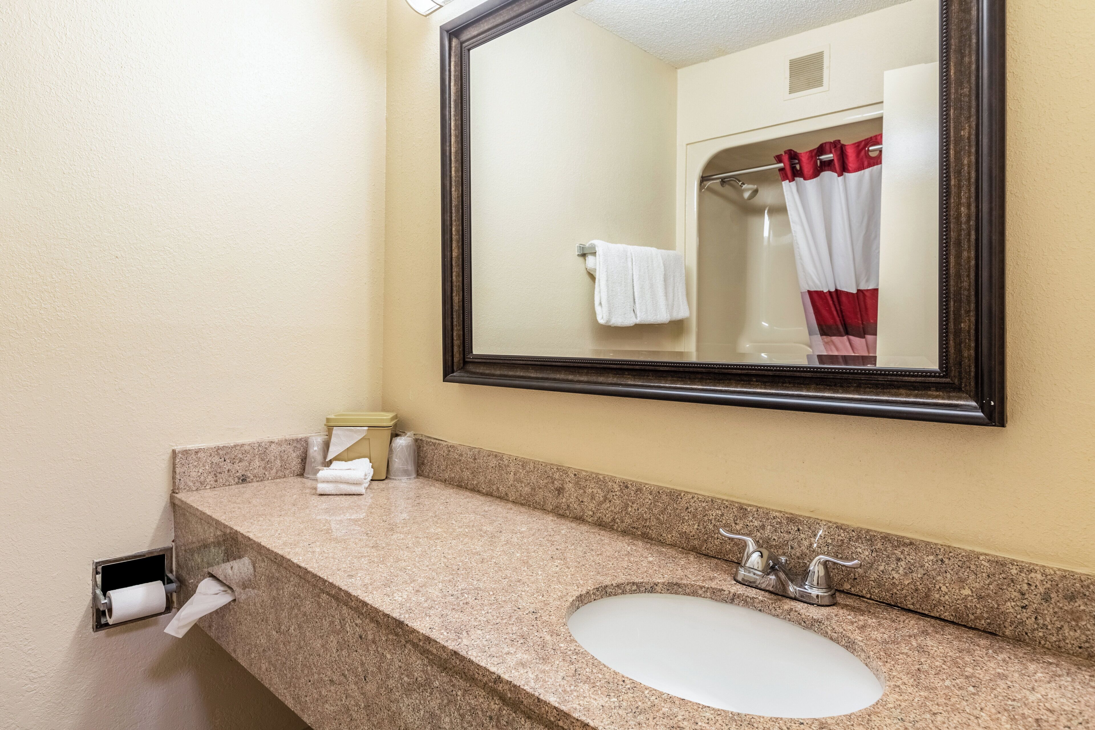 A bathroom with a granite countertop, a white sink, a mirror, and a shower with red curtains.