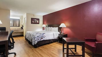 A hotel room with a bed, bedside lamps, a desk, a chair, and a red accent wall.