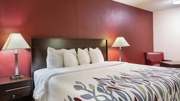 A hotel room with a large bed, two bedside lamps, a red wall, and a small desk with a chair.