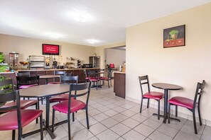 Un restaurante con varias mesas y sillas, una zona de cocina y un letrero que indica disponibilidad de Wi-Fi gratuito.