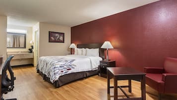 A hotel room with a bed, bedside lamps, a desk, a chair, and a red accent wall.