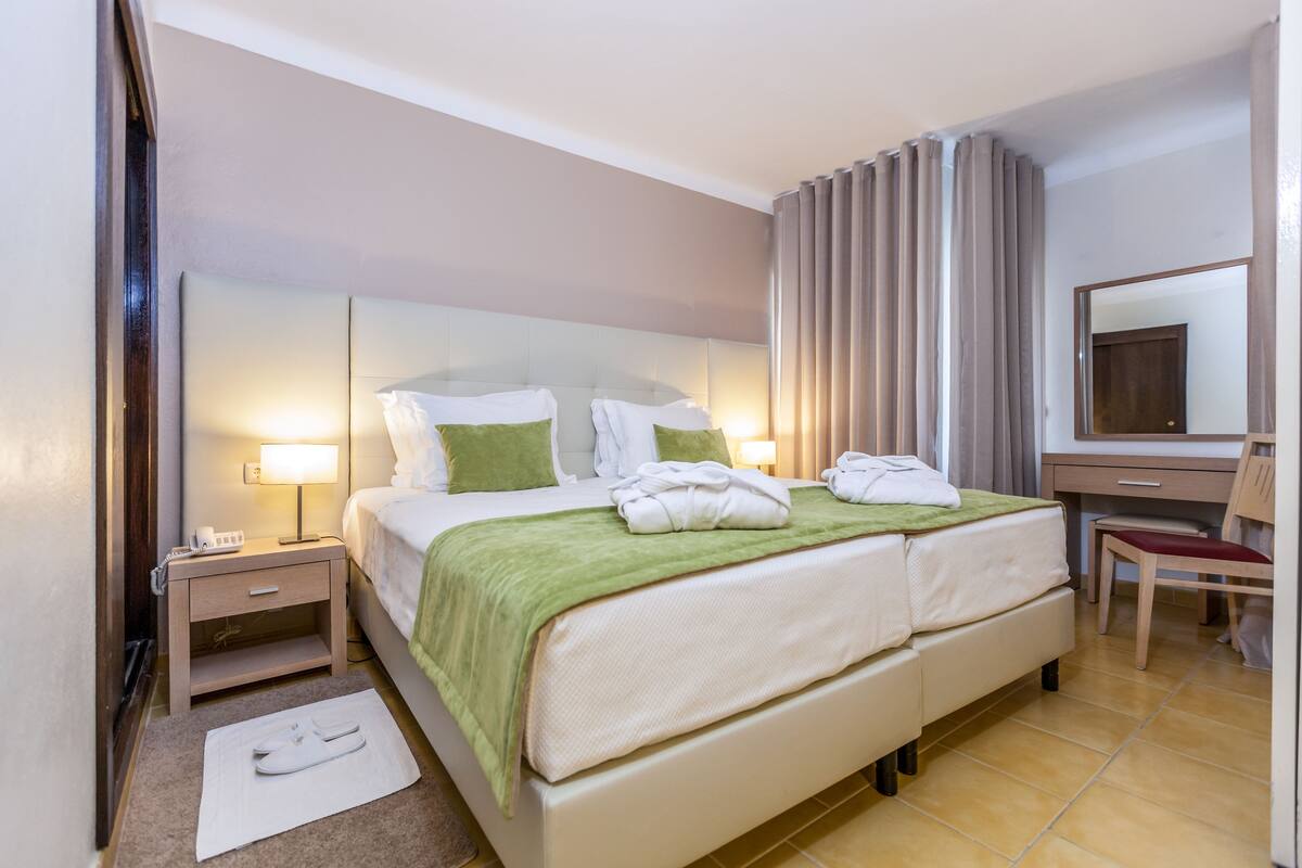 Een hotelkamer met een groot bed, twee nachtkastjes met lampen, een stoel, een bureau en een spiegel.