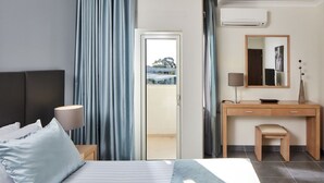 Quarto de hotel com cama, escrivaninha, cadeira, luminária e janela com cortinas.