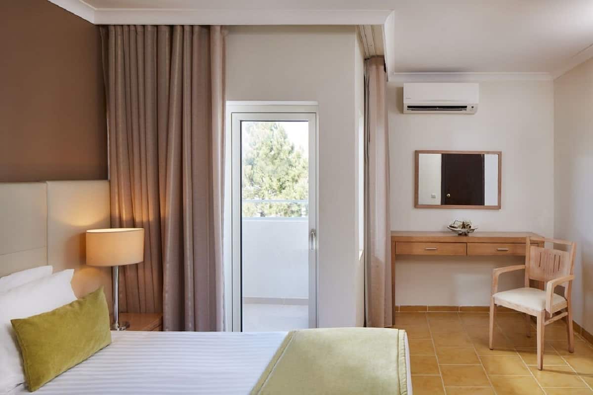Een hotelkamer met een bed, een bureau, een stoel, een lamp, airconditioning en uitzicht op het landschap.