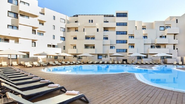 Um hotel com uma grande área de piscina, espreguiçadeiras e guarda-sóis.