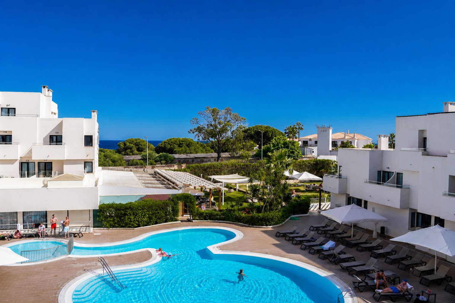 Um resort com piscina, áreas de descanso e vista para o mar.