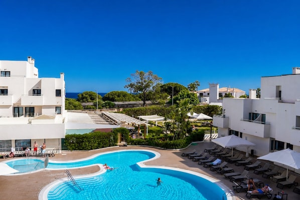 Un resort con piscina, zonas de descanso y vistas al mar.