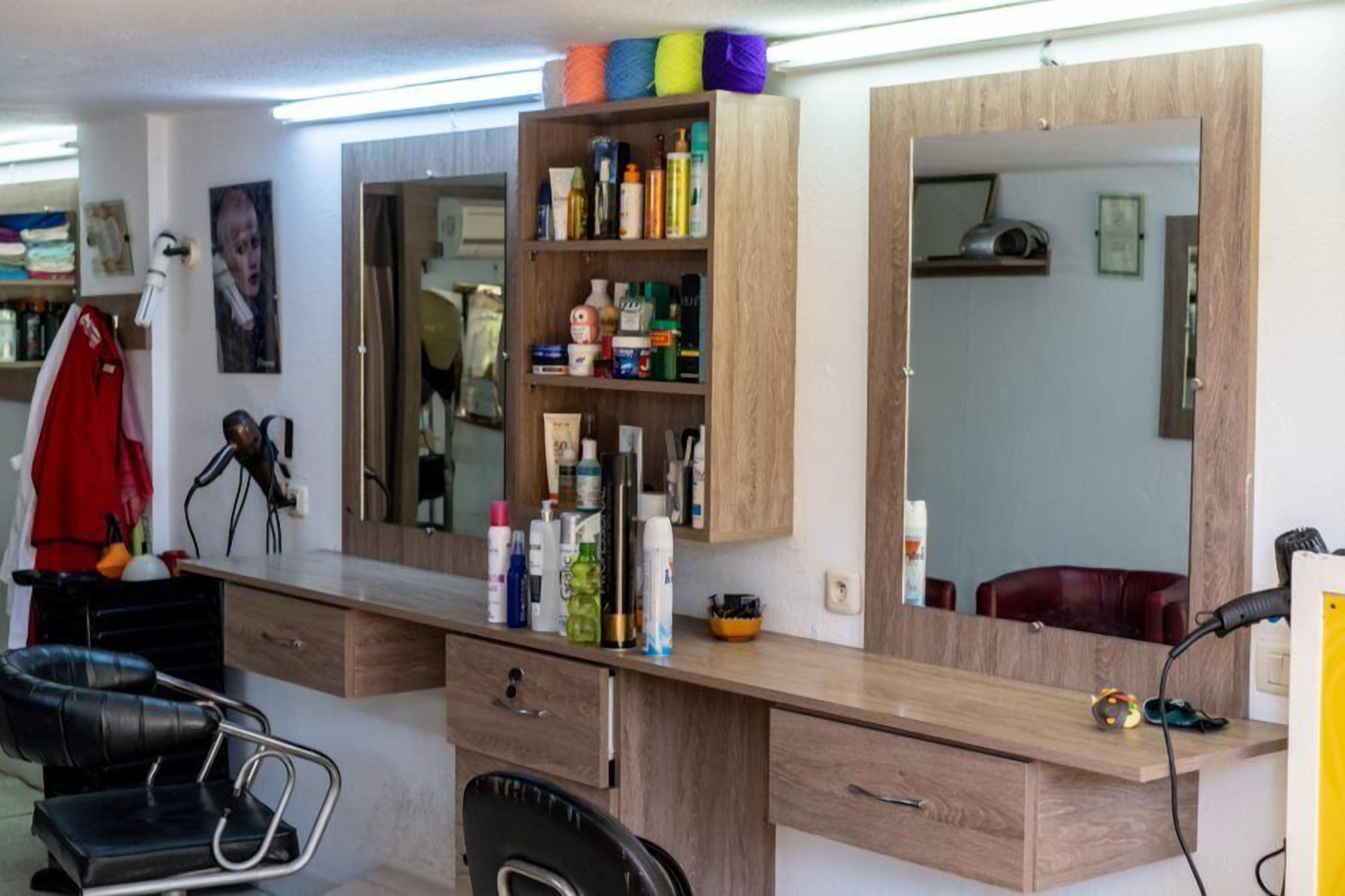 Un salón con mostrador de madera, estantes con productos para el cabello, un espejo y una chaqueta roja colgada en la pared.