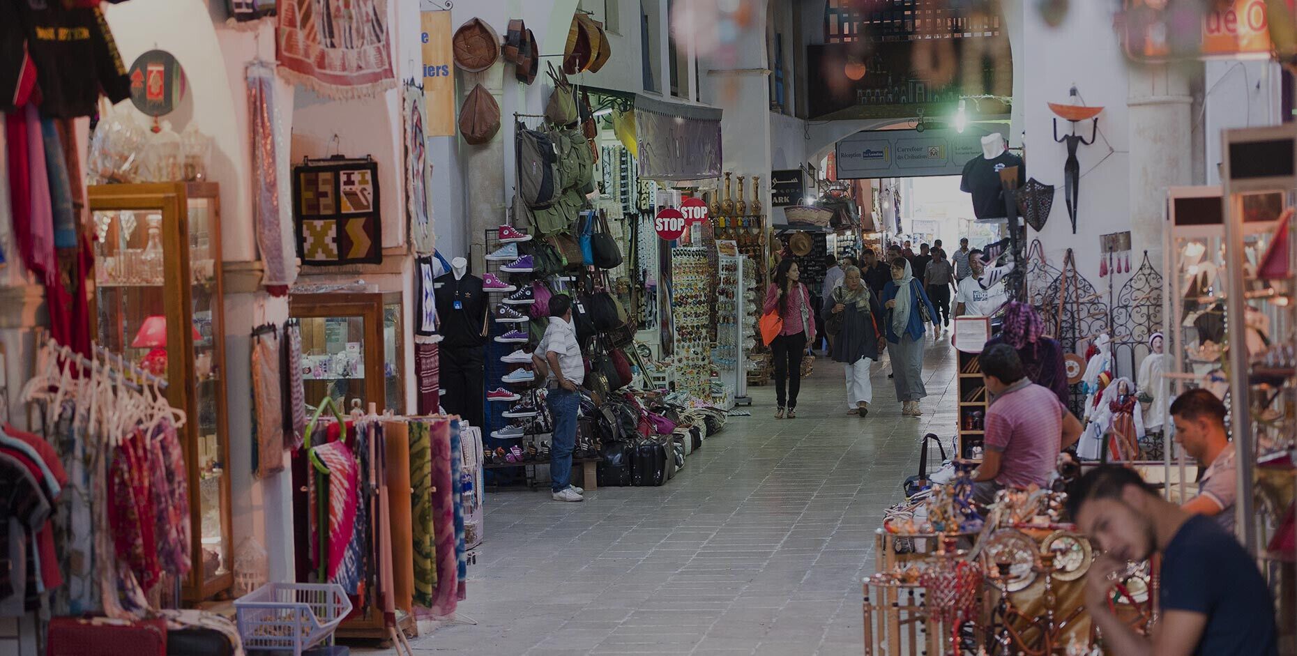 A bustling indoor market with various stalls selling textiles, bags, and accessories.