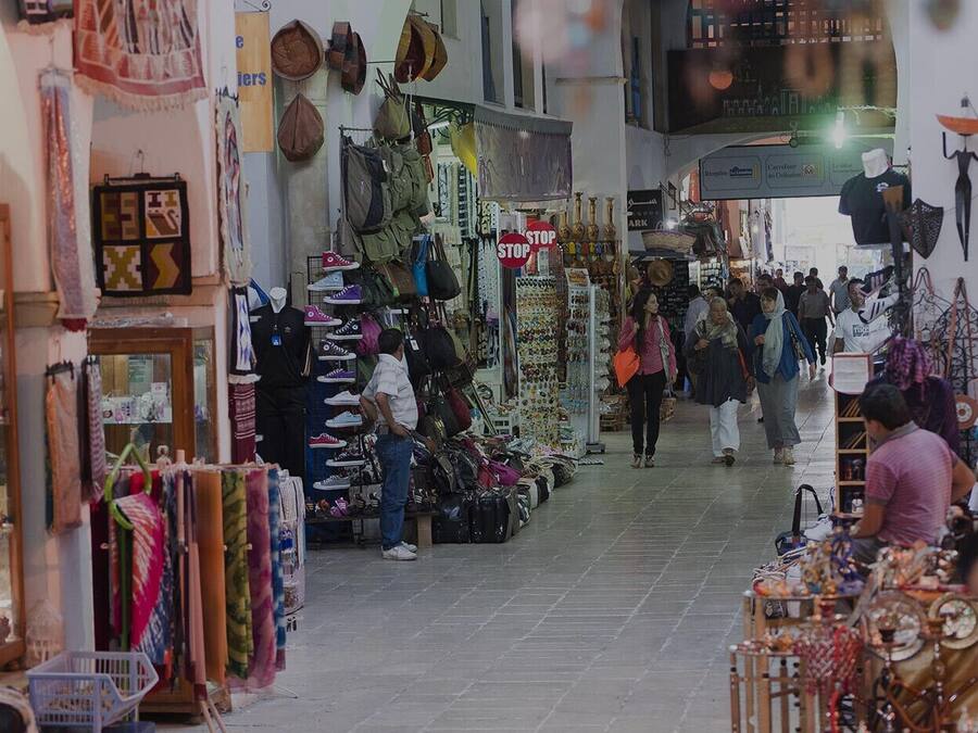 A bustling indoor market with various stalls selling textiles, bags, and accessories.