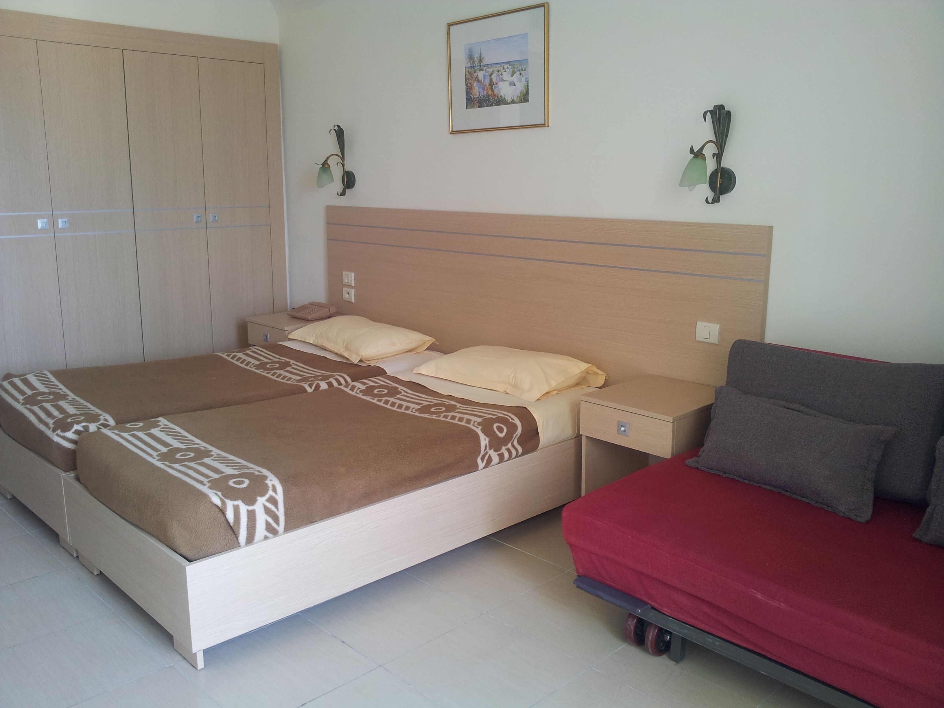 A bedroom with a bed, a nightstand, a dresser, and a red sofa.