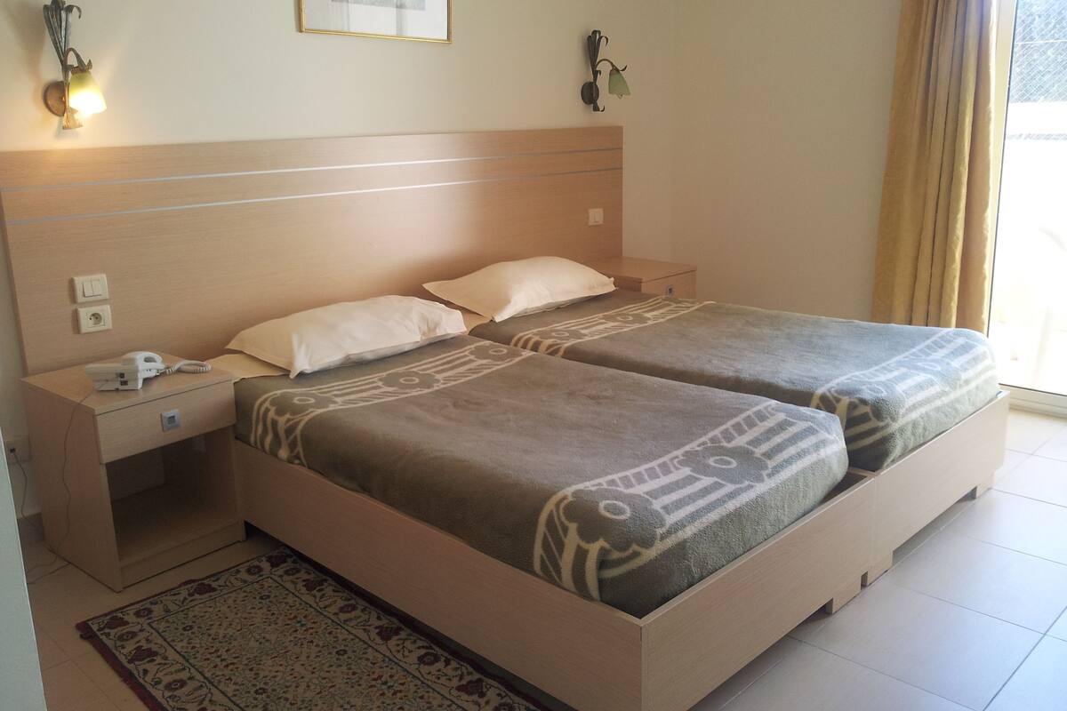 Una habitación de hotel con dos camas, una mesita de noche, un teléfono y una lámpara fijada a la pared.