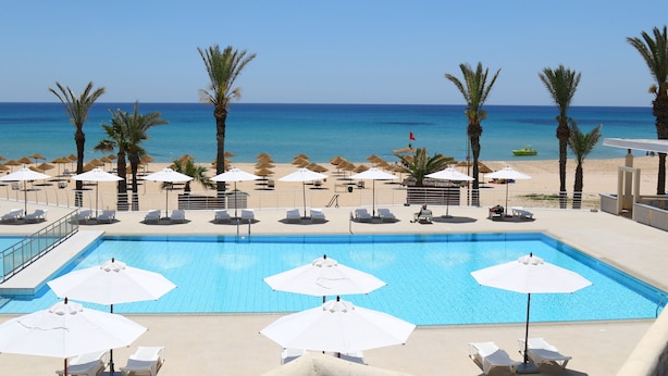 Zona de piscina con sillones de descanso y sombrillas, vista despejada a la playa y mar tranquilo.