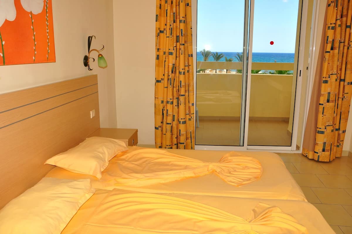 Un dormitorio con cama, mesita de noche, un cuadro y vista al mar a través de una puerta corrediza.