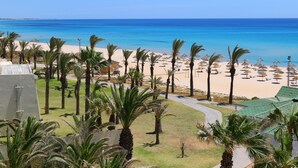 Una playa con palmeras, sombrillas y un mar azul y transparente.