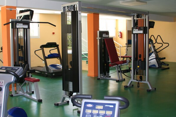 Une salle de sport équipée de divers appareils d’exercice, notamment des tapis de course, des appareils de musculation et un banc.