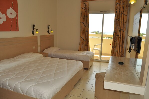 Habitación de hotel con dos camas, una mesita, un televisor y un balcón con vistas.