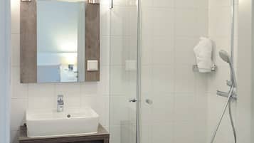 Une salle de bain moderne avec une douche à parois de verre, un lavabo blanc et un miroir agrémenté de luminaires fixés au mur.